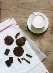 Chocolate cookies, pieces of chocolate and a cup of cocoa or coffee with milk on a wooden background. Rustic style.