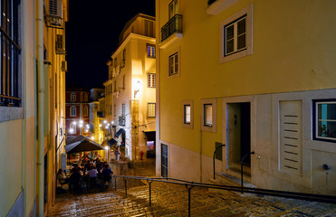 Lisbon, Portugal. Nighttime streets with stone stairs and restaurants under street lamps with evening illumination. Old downtown city centre.