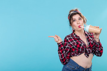 Cute charming young woman in retro clothes is drinking a cocktail from a straw posing against a...