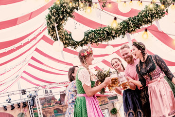Gruppe von 5 Freunden auf dem Oktoberfest in Trachten stoßen mit Maß Bier an 