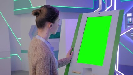 Green screen, mockup, science, copyspace, template, chroma key, technology concept. Woman looking at vertical green display of interactive kiosk at exhibition or museum with futuristic sci-fi interior