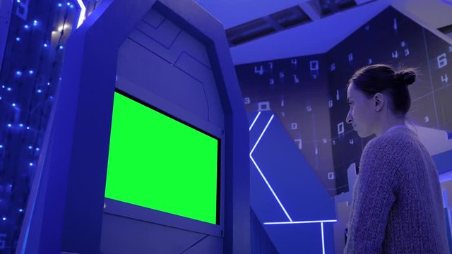 Green screen, mockup, science, copyspace, template, chroma key, technology concept. Woman looking at blank green display of interactive kiosk at exhibition or museum with futuristic sci-fi interior