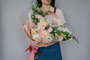 Very beautiful florist woman holding a beautiful colorful blooming bouquet of flowers on a gray wall background.