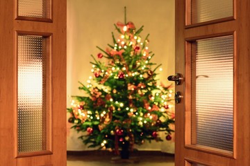 Half opened door into the cozy home  interior with beautiful Christmas tree - blured lights