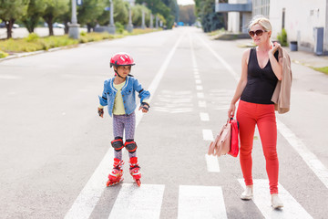 Young mother with her 5 years old daughter rollerskating in park