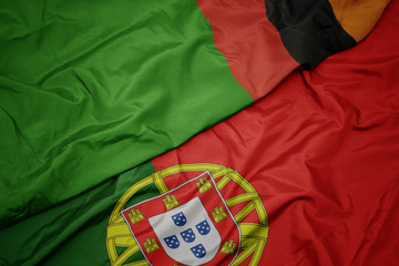 waving colorful flag of portugal and national flag of zambia.