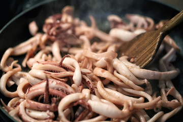 Close-up frying pan cooking baby squid and octopus. Wooden kitchen spatula mixing ingridients while preparing frying calamari traditional italian seafood meal
