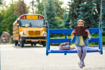 little girl reads near school. Pupil of primary school with book in hand. Beginning of lessons. First day of fall.