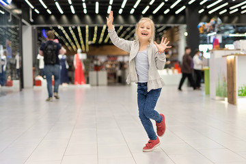 Cute adorable caucasian blond girl enjoy walking at shopping mall. Beautiful cheerful child having fun and running at retail fashion departmant store. Happy childhood concept