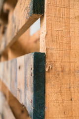 Close up of a light brown wooden pallet with blue markings from usage and shot with selective focus on the side board closest to the viewer.