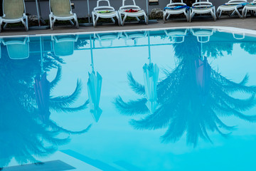 Blue water in an artificial pool. Background. On the water surface are visible reflections of palm trees and beach umbrellas. Copy space.