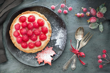 Homemade tart with custard and fresh raspberries, served on black plate sprinkled with sugar