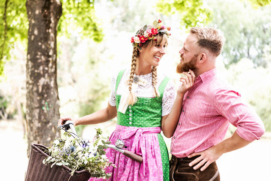 Junge verliebtes Paar mit Fahrrad auf dem Weg zur Festwiese in Trachten 
