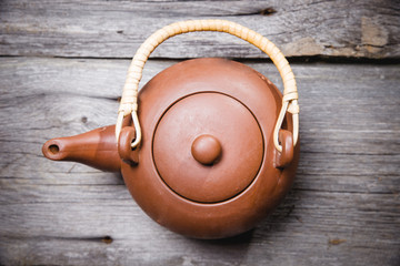 Old clay teapot stands on a wooden shelf.