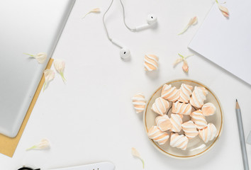 Woman workspace with tablet, flower petals, headphones, and marshmallows on white background. top view