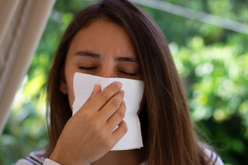 Health and medicine - Young woman sneezing in the woods with a handkerchief.