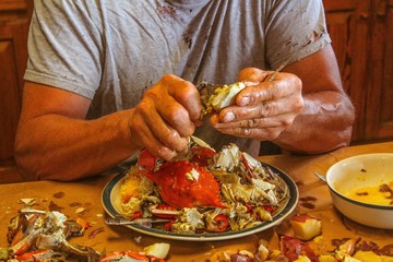 Older man with very strong looking hands eating a crab at a traditional Cajun seafood boil served steaming hot on brown paper