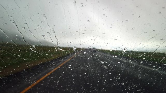A car is driving in a storm. Rain drops are coming down on the windshield.