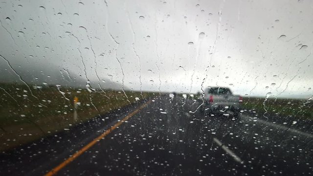 A car is driving on the freeway. Heavy rain is coming down on the car's windshield.