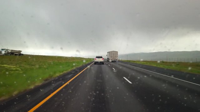 A car is driving near two cars on a freeway. Rain drops are seen dripping on the windshield.