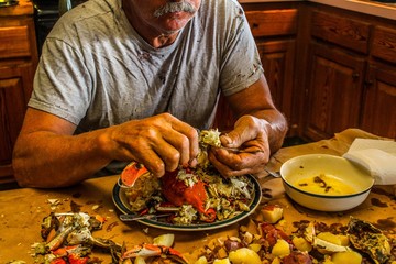 Older man with very strong looking hands eating a crab at a seafood boil