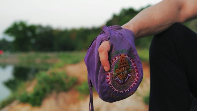 Close-up, Man Reads Mantra on the Rosary in Pouch Sitting on the Shore of a Pond