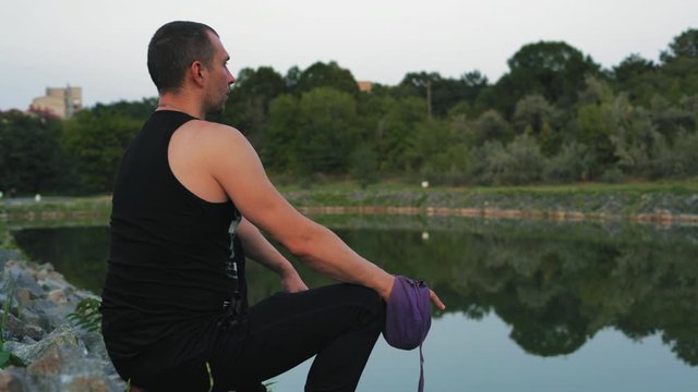 Religious Man Reads Mantra Sitting on the Lake Shore Holding Pouch with Rosary in Hand
