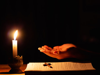 Human praying to the GOD while with a crucifix symbol with lighting candle at night time.