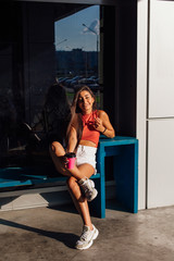 Stylish happy young brunette woman wearing white shorts and sneakers holding pink cup of coffee to go.