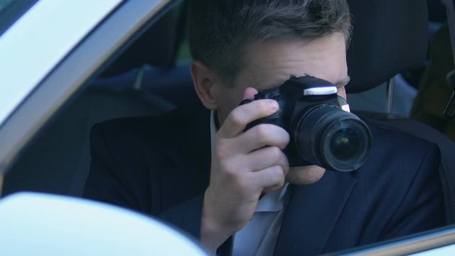 Young man secretly taking photo sitting in car, spying detective, journalist