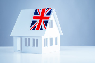 Immigration abroad. Miniature house with the flag of great Britain. Leave for permanent residence in the United Kingdom. Resettlement to England. Acquisition of real estate in England.