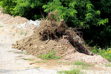 Small pile of construction material and dried branches left on one side of local gravel road surrounded with grass and trees on warm sunny summer day