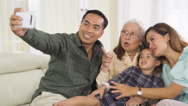 Happy elderly woman taking picture with her son, daughter, and granddaughter in the living room at home. Shot in 4k resolution