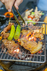 Human hand using tongs while grilling meat on flaming stove