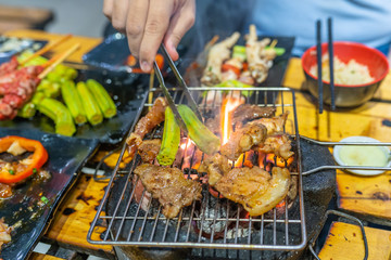 Human grilling okra and marinated meat on flaming charcoal stove