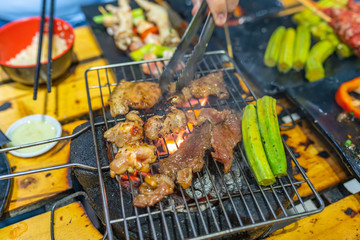 Human hand using tongs and grilling meat on charcoal stove