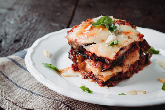 tradicional Parmigiana di melanzane: baked eggplant - italy, sicily cousine.Baked eggplant with cheese, tomatoes and spices on a white plate. A dish of eggplant is on a wooden table