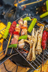 Grilling pork skewers, chicken leg and vegetables on charcoal stove