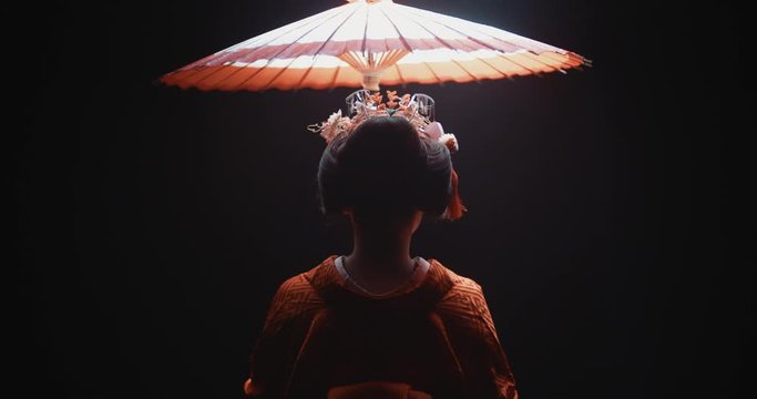 Japanese girl in traditional kitsune clothing standing under red umbrella, isolated on black background - culture, tradition concept 4k footage