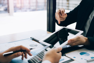 Managers are using tablets to analyze sales cost reports and explain summary reports to employees calculate and record summary information data in the office.