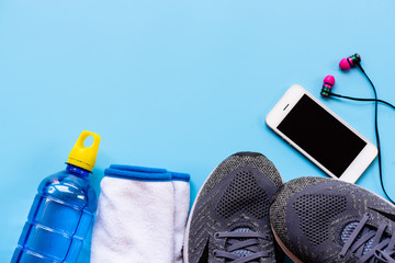 Running tools on blue background.Sport shoes, mobile phone, drinking water bottle and blue tooth ear plug equipment for running healthy sport man.Indoor sport accessories and copy space.