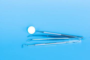 Different dental tools for demonstration patient.Mirror, sickle probe and surgical forceps on blue...