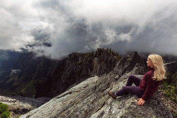 Adventurous Girl on top of a rugged rocky mountain during a cloudy summer morning. Taken on Crown Mountain, North Vancouver, BC, Canada.