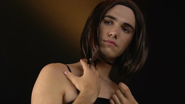 Transvestite in female wig and black dress admiring appearance, cross-dressing