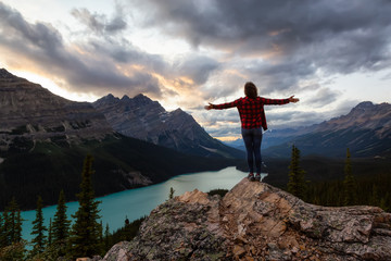 Adventurous girl with open arms standing on the edge of a cliff overlooking the beautiful Canadian Rockies and Peyto Lake during a vibrant summer sunset. Taken in Banff National Park, Alberta, Canada.