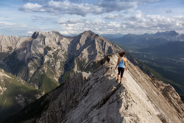 Adventurous Girl is hiking up a rocky mountain during a cloudy and rainy day. Taken from Mt Lady MacDonald, Canmore, Alberta, Canada.