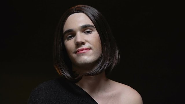 Transvestite applying lip gloss smiling camera, crossdressing, black background