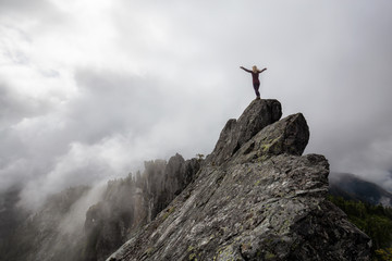 Adventurous Girl with Open Arms on top of a rugged rocky mountain during a cloudy summer morning. Taken on Crown Mountain, North Vancouver, BC, Canada.