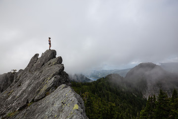 Adventurous Girl on top of a rugged rocky mountain during a cloudy summer morning. Taken on Crown Mountain, North Vancouver, BC, Canada.