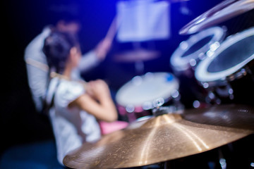 Selective focus to cymbals of drum set with blurry kid learning and play drum set with teacher in music room. The concept of musical instrument.